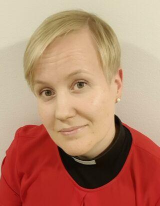 Kaisa Yletyisen kasvokuva papin pantapaidassa ja punaisessa paidassa