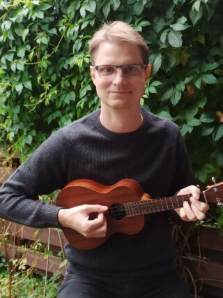 Asiantuntija Timo-Matti Haapiaisen kasvokuva, käsissä ukulele, taustalla vihreä villiviiniköynnös