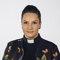 Henkilökuva saamelaistyönyhdyshenkilö Hanni Raiskiosta papin pantapaidassa ja kuvioidussa mustassa jakussa