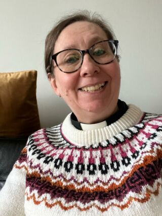 Pastori Kirsi Muurimäki papinpaidassa ja värikkäässä kaarrokekuvioisessa villapaidassa.